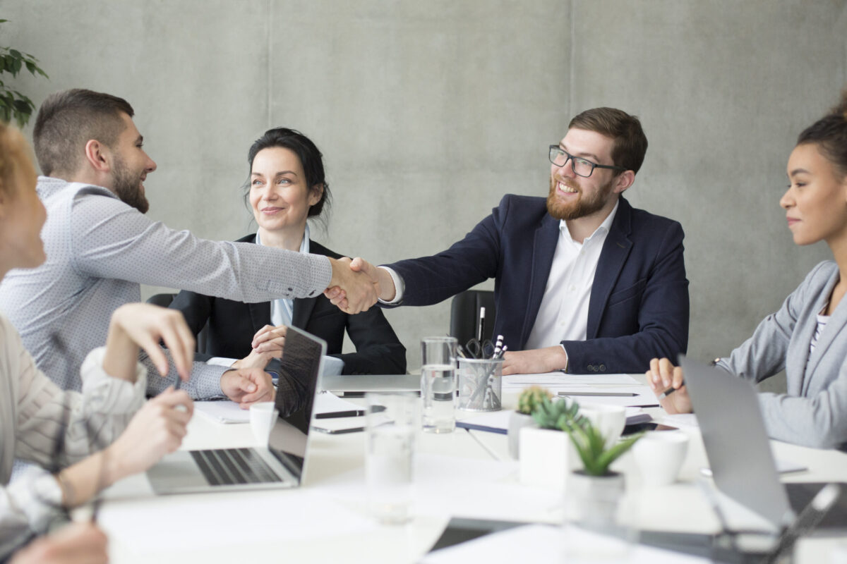 Male boss shaking hands with employee at meeting, congratulatng with new job